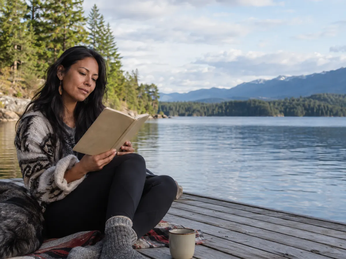 Kvinne leser en bok på en brygge ved et fjellvann